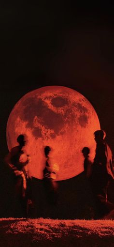 people are walking in front of the full moon with red light on it's face