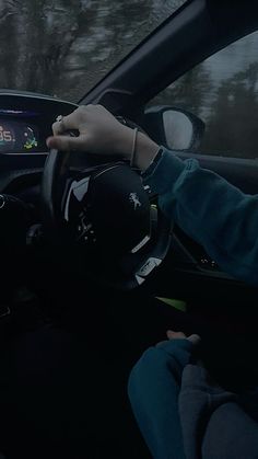 a person sitting in a car with their hand on the steering wheel while holding onto an electronic device