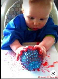 a baby in a highchair playing with a brush and splattered ball