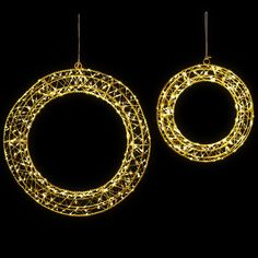 two circular christmas lights hanging from strings on a black background, with the light shining through them