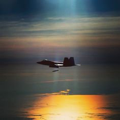 an airplane flying over the ocean at sunset