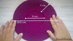 two hands are holding a purple crochet dishcloth on a white table top