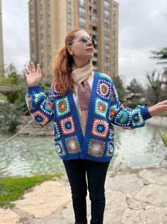 a woman standing in front of a body of water wearing a blue crocheted cardigan