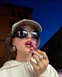 a woman wearing sunglasses and a hat is holding a pink tube in her mouth while standing outside at night