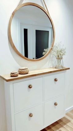 a white dresser with a round mirror on it's top and wooden drawers below