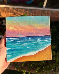 someone is holding up a small piece of art that looks like the beach at sunset