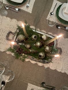 the table is set with silverware, candles and pine cones on top of it