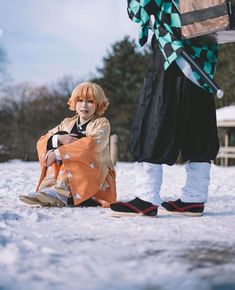 a person sitting in the snow next to another person with an orange and black bag