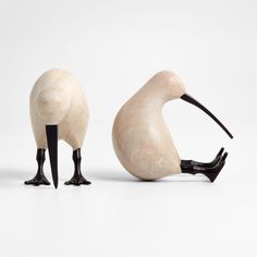 two wooden birds standing next to each other on top of a white surface with black legs