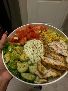 a person holding a bowl filled with chicken, vegetables and dressing