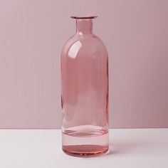 a pink glass bottle sitting on top of a white table next to a pink wall