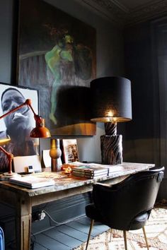 a desk with two lamps on top of it next to a painting and lamp shade