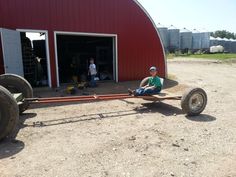 a man sitting on the ground in front of a red barn with two large wheels