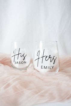 two wine glasses with the words his and hers on them sitting next to each other