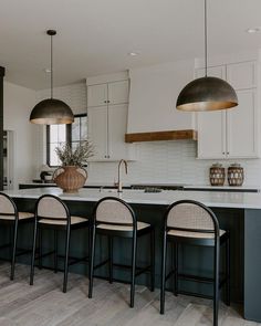 a kitchen with white cabinets and black countertops, two chairs at the center island