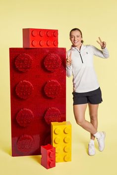 a woman is posing next to a lego block and giving the peace sign with her right hand