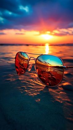 a pair of sunglasses sitting on top of a beach next to the ocean at sunset