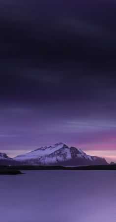 the mountains are covered in snow as the sun goes down over the water and it's purple hues