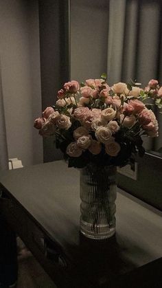 a vase filled with pink flowers sitting on top of a wooden table next to a mirror