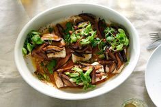 a white bowl filled with mushrooms and greens next to a plate of food on a table