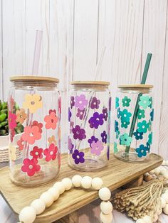 three mason jars with flowers painted on them and straws in the bottom one is empty