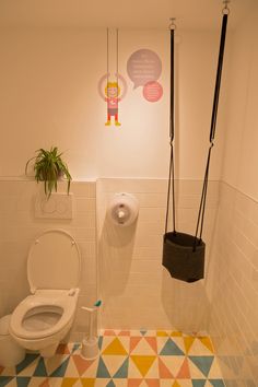 a bathroom with a toilet, plant and two hanging objects on the wall above it