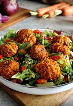 a salad with meatballs and lettuce in it on a wooden cutting board