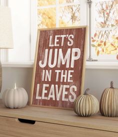 a sign that says let's jump in the leaves next to some pumpkins