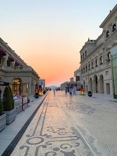 the sun is setting on an empty street with people walking down it and shops lining both sides