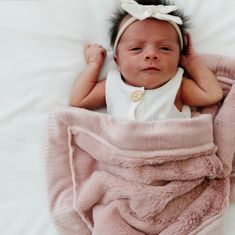 a baby wrapped in a pink blanket on top of a white sheet and wearing a headband