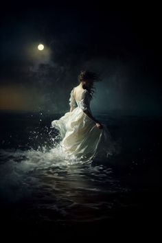 a woman in a white dress is standing in the water at night with her back to the camera