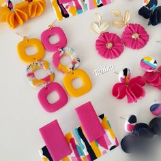 several pairs of colorful earrings are displayed on a white surface with letters and flowers in the background