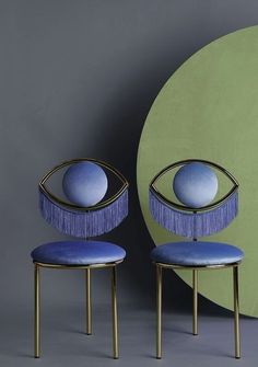 two blue chairs with fringes on them in front of a green wall and circular object