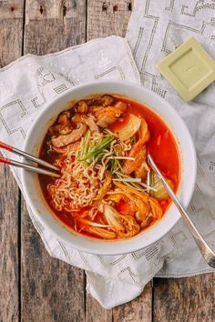 a bowl of soup with noodles, meat and veggies on a wooden table