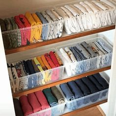 an organized closet filled with folded shirts and other items in clear bins on wooden shelves