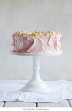 a pink frosted cake sitting on top of a white cake platter next to a napkin