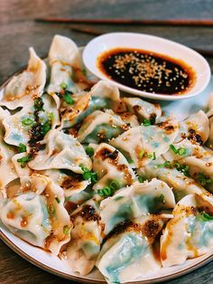 a white plate topped with dumplings next to a bowl of dipping sauce on top of a wooden table