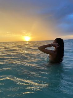 a woman sitting in the ocean at sunset