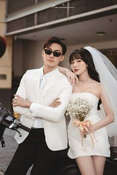 a man and woman dressed in white standing next to each other on a motorcycle wearing sunglasses