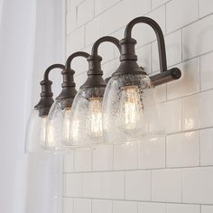 three light bathroom fixture with clear glass shades on the bottom and sides, hanging from a white tile wall