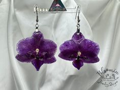 purple flower earrings with pearls hanging from them on a white cloth covered background, closeup