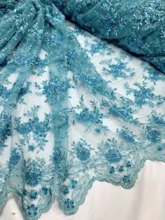 a blue lace with flowers on it is laying on a white sheet that has been folded over