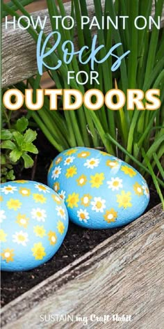 two painted rocks sitting next to each other on top of a wooden bench with grass and flowers