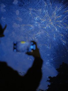 a person taking a photo with their cell phone while fireworks go off in the sky