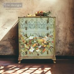 an old dresser painted with flowers and fruit on it's side, sitting against a wall