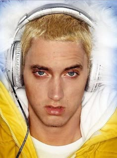 a young man with headphones on his ears looking at the camera while wearing a yellow jacket