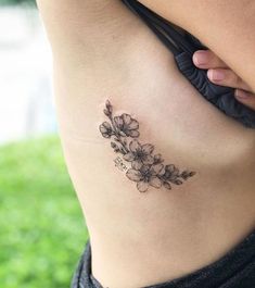 a woman's lower back tattoo with flowers on her left side ribcage