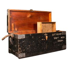 an old wooden box with writing on the lid and rope attached to it's sides