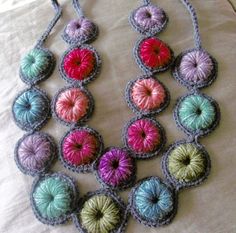 a multicolored crocheted necklace is displayed on a bed