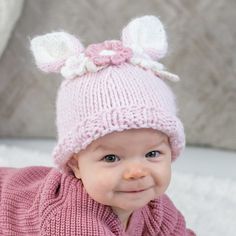 a smiling baby wearing a pink knitted hat with white bows on it's head